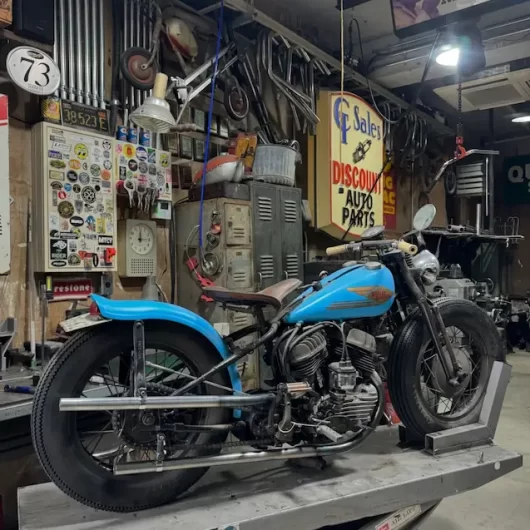 Heiwa Motorcycle custom Harley-Davidson flathead bobber with blue tank inside vintage motorcycle workshop