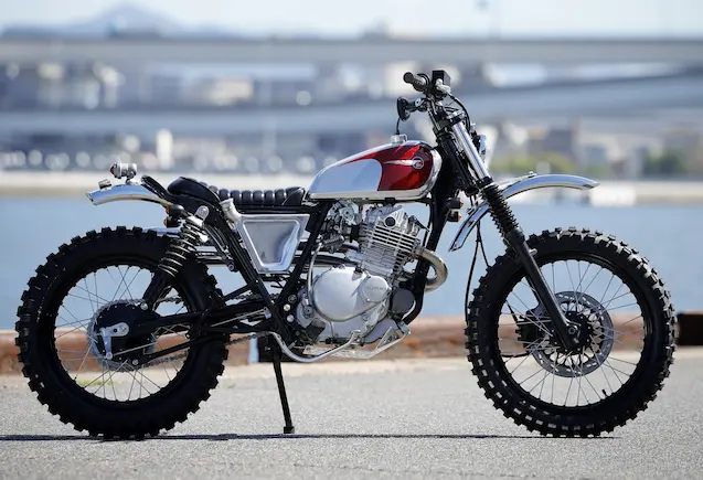 Heiwa Motorcycle custom Suzuki Grass Tracker 250 scrambler with red and white tank and off-road tires side view